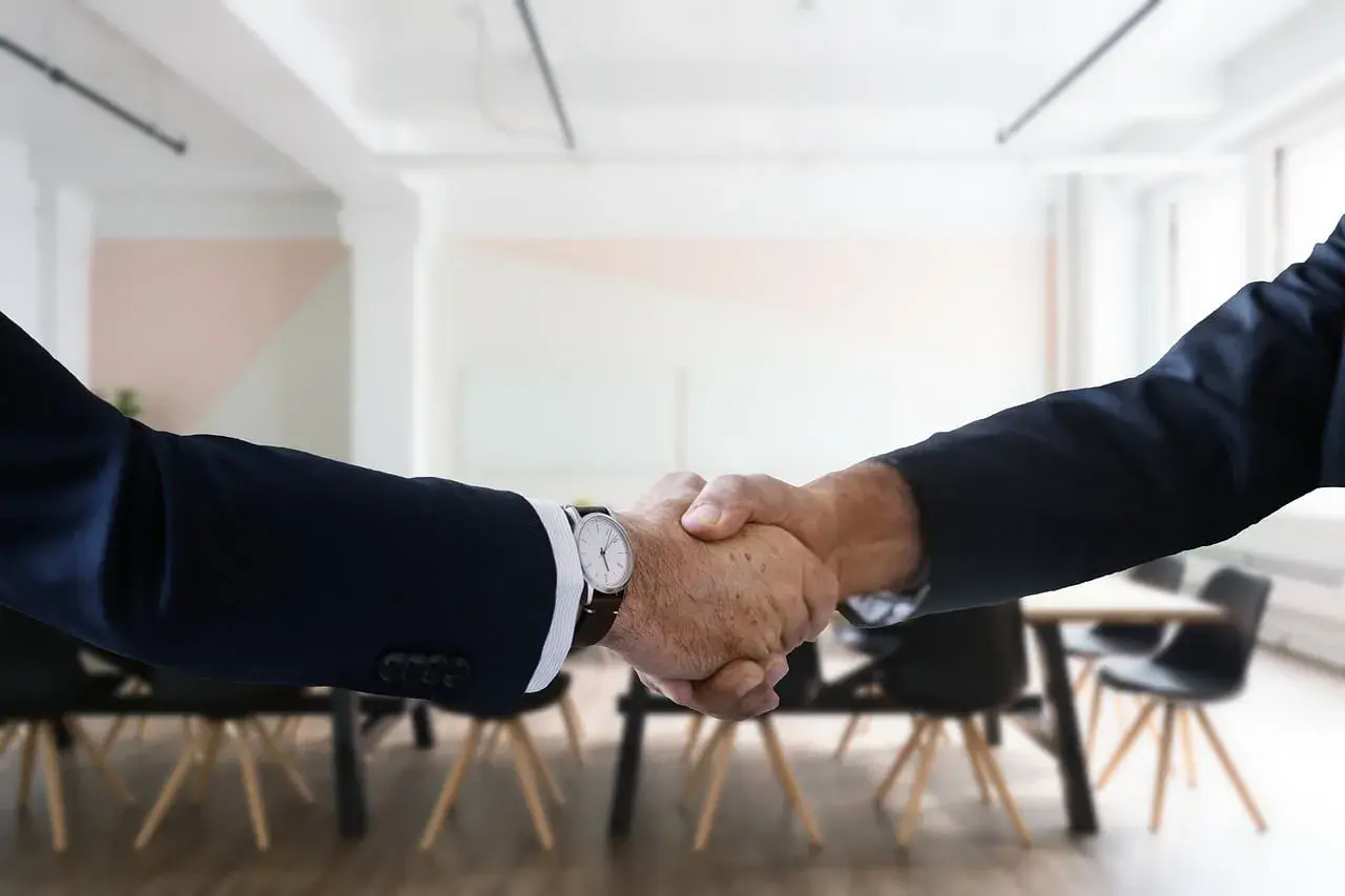 Two men in suits shake hands, a gesture of how to be professional with coworkers.