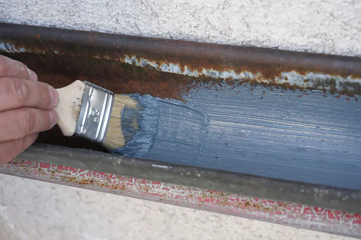 Hand streicht mit Pinsel graue Farbe auf rostige Dachrinne zum dachrinne abdichten.