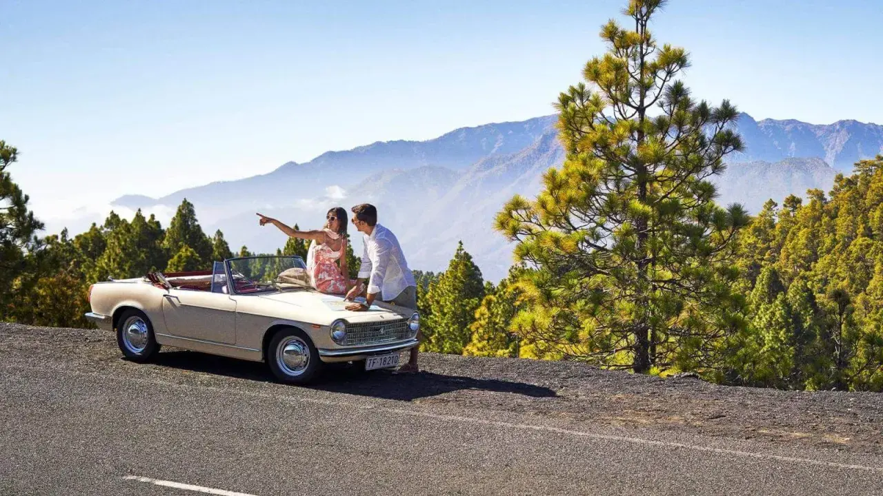 Pareja planeando sus rutas en coche por La Palma, con un descapotable y un paisaje montañoso de pinos.