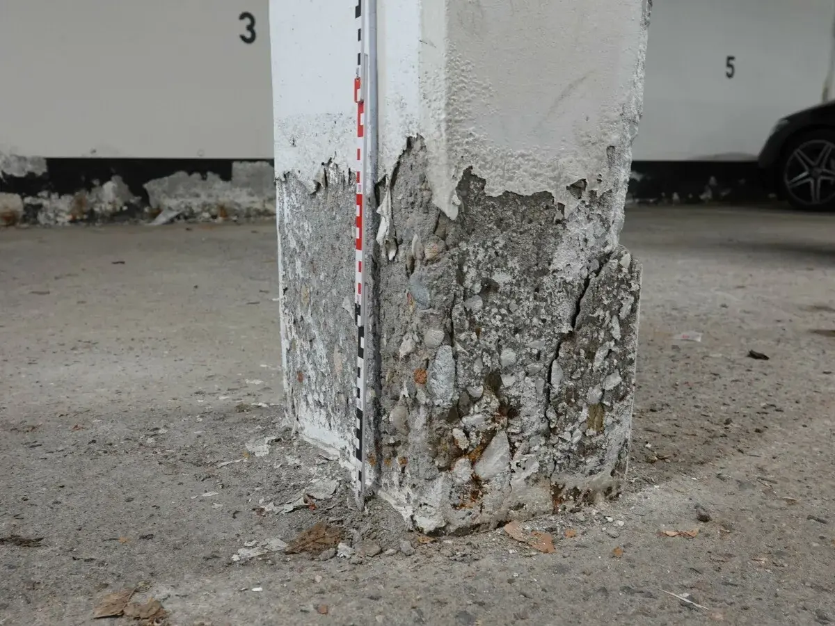 Betonsäule mit starker Abplatzung und Rissen, Messlatte zur Schadensdokumentation. Die STB Decke ist hier stark beschädigt.