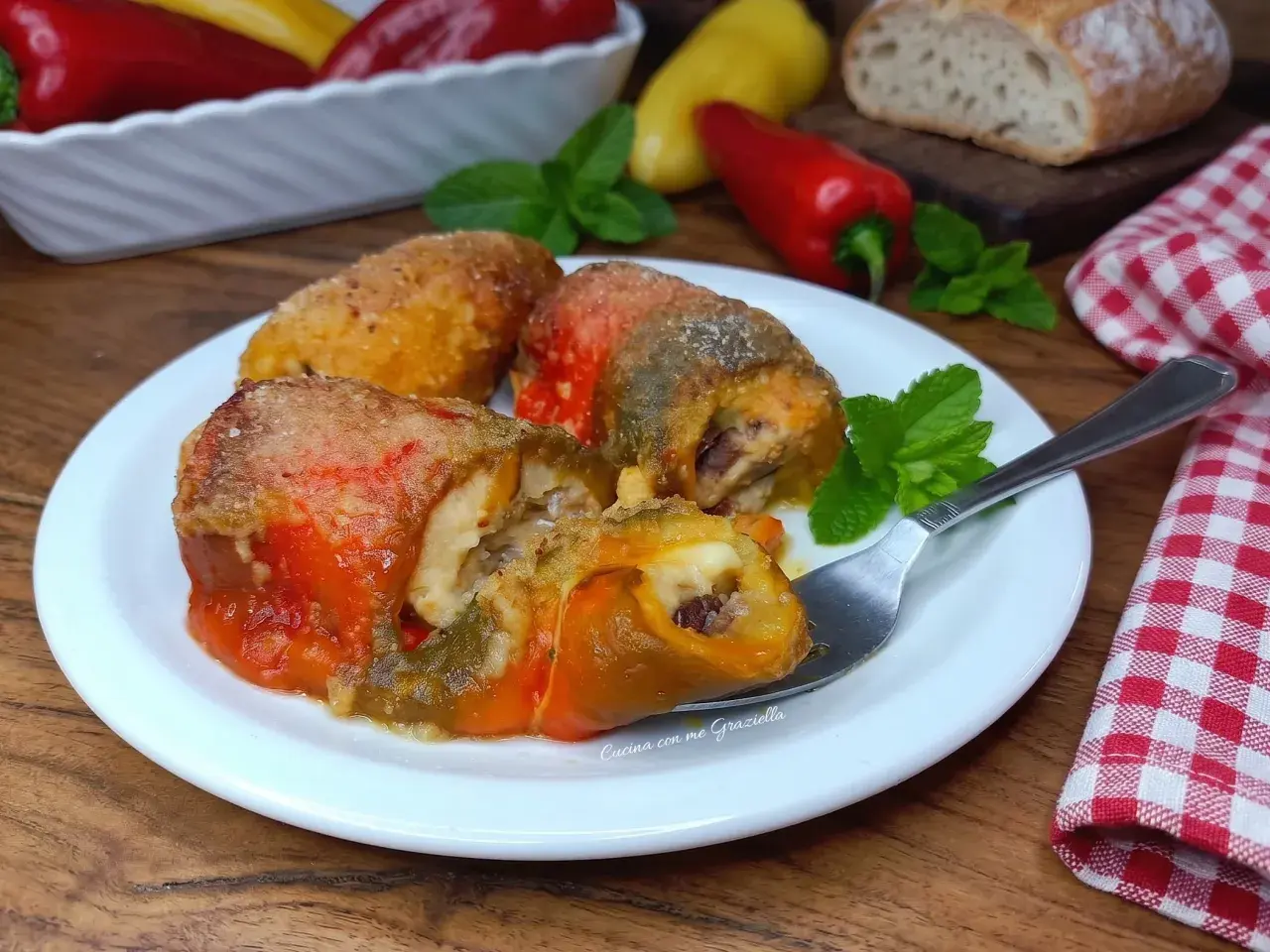 Involtini di peperoni ripieni, dorati e succulenti, serviti su un piatto bianco con menta fresca.