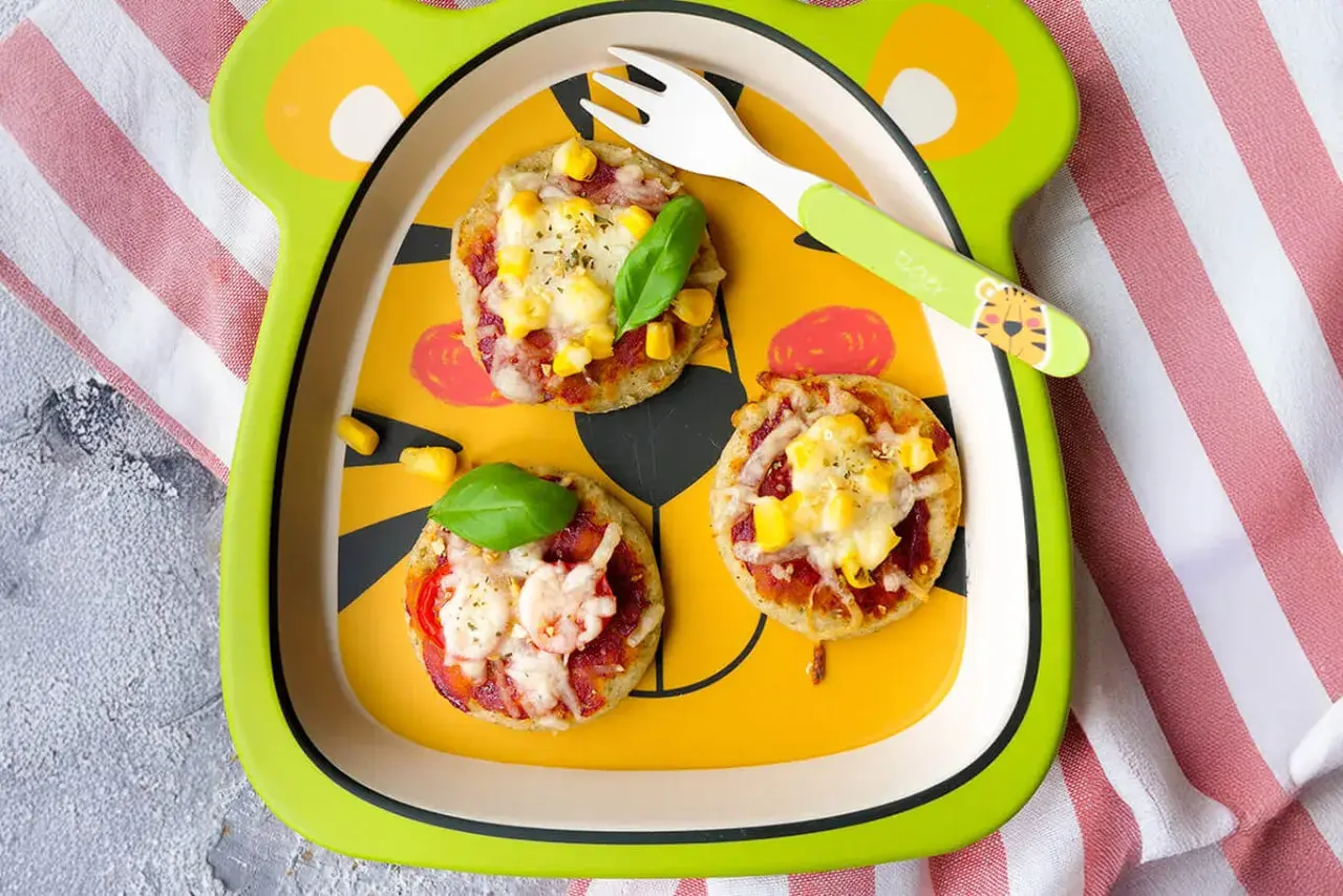 Schneller Pizzatag mit Quark: Kleine Mini-Pizzen mit Mais und Käse auf einem lustigen Teller, bereit zum Genießen.
