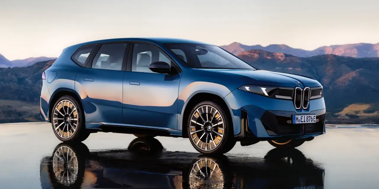 La BMW Neue Klasse blu metallizzato, con riflessi del tramonto, si staglia su uno sfondo montuoso.