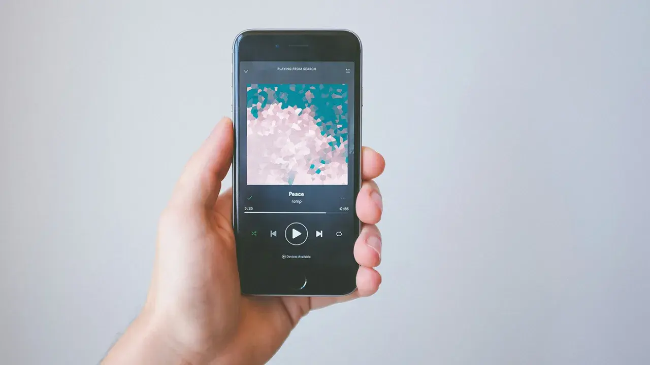 A hand holds a smartphone displaying the Spotify app, showing the song "Peace" by ramp. This image illustrates how to get music on Spotify.