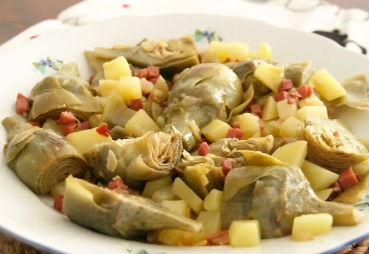 Plato de alcachofas tiernas y patatas cortadas en cubos, salpicado con trocitos de jamón. Un manjar casero.
