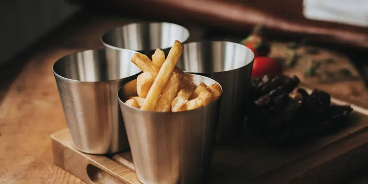 Tre metallbägare med hemmagjorda pommes frites. En bägare är fylld med gyllene pommes.