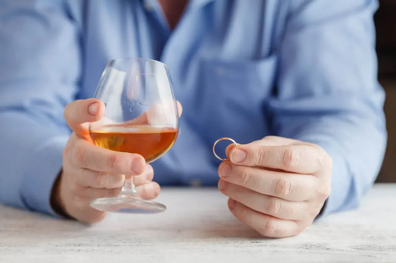 Mężczyzna trzyma kieliszek z alkoholem i obrączkę. Rozważania o rozdzielności majątkowej a alimentach na dziecko z poprzedniego związku.