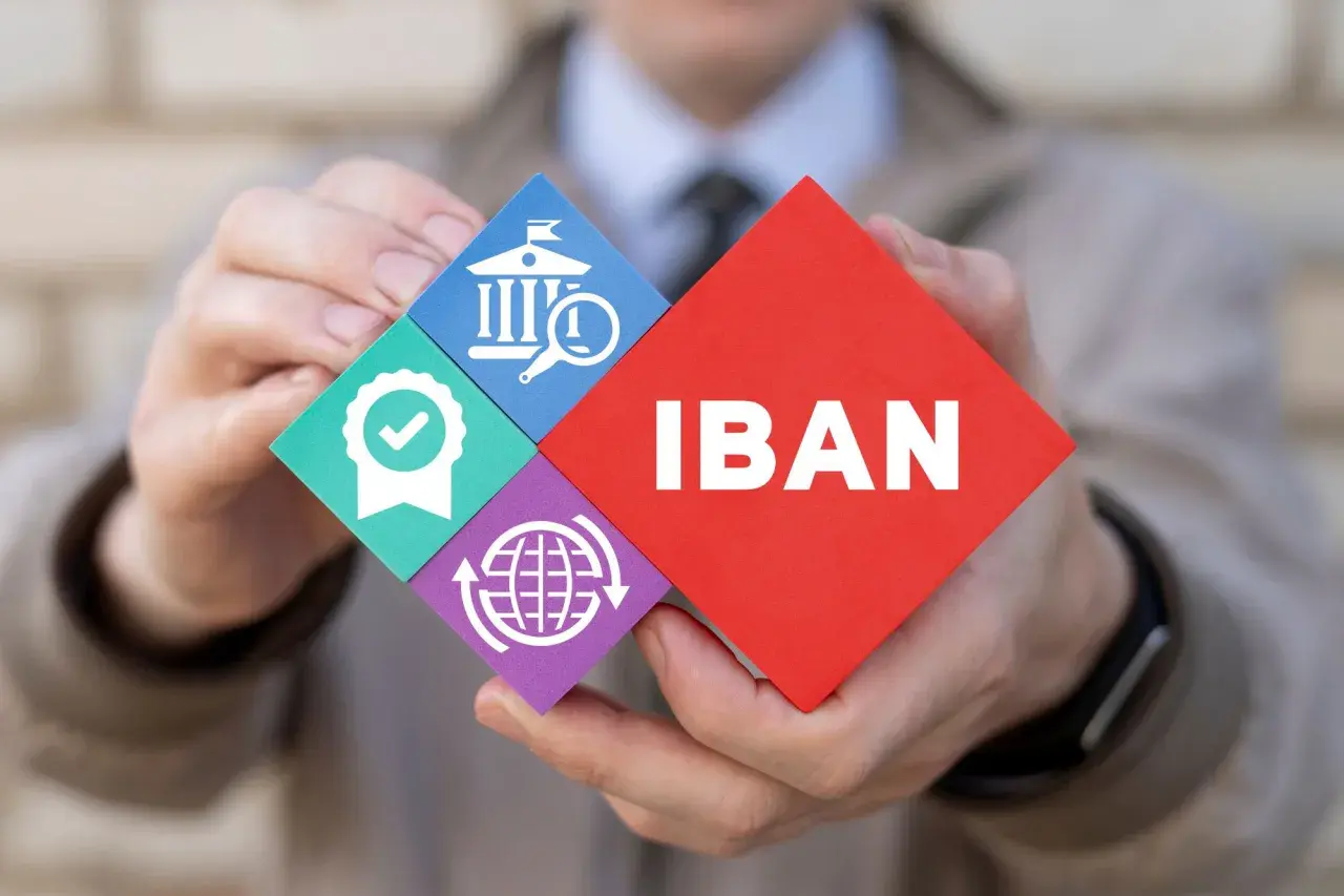 Ręce trzymają puzzle z napisem IBAN i ikonami: bank, pieczęć jakości, globalny zasięg.