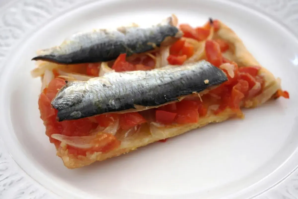 Rebanada de masa con tomate, cebolla y dos sardinas enteras, un plato que recuerda a las sardinas San Juan.