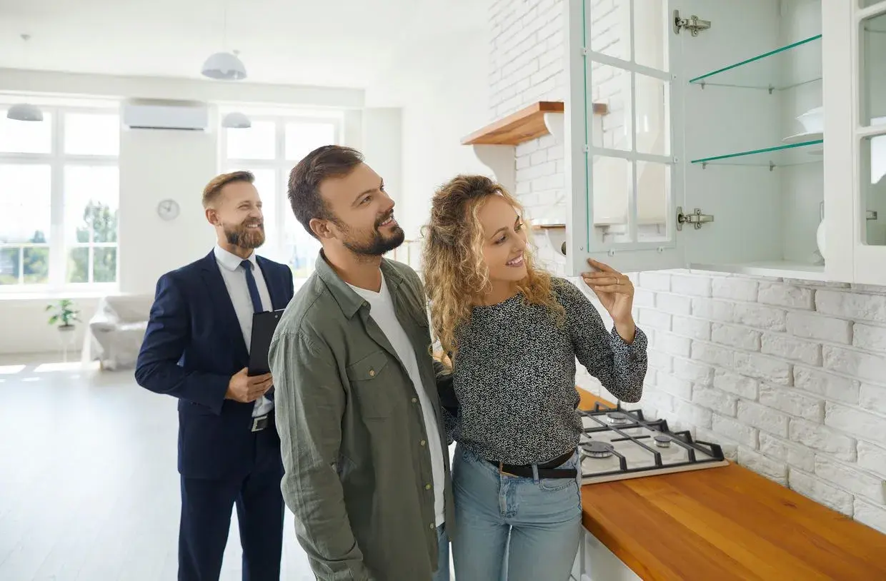 Couple inspecte une cuisine lors d'un état des lieux avant signature notaire. Un agent immobilier les accompagne.