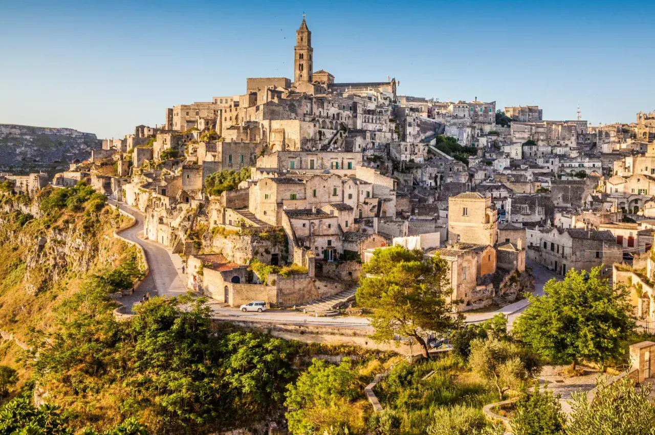 Matera: zobacz starożytne kamienne domy i kościół na wzgórzu. Wąskie uliczki i zielone zbocza tworzą malowniczy krajobraz.