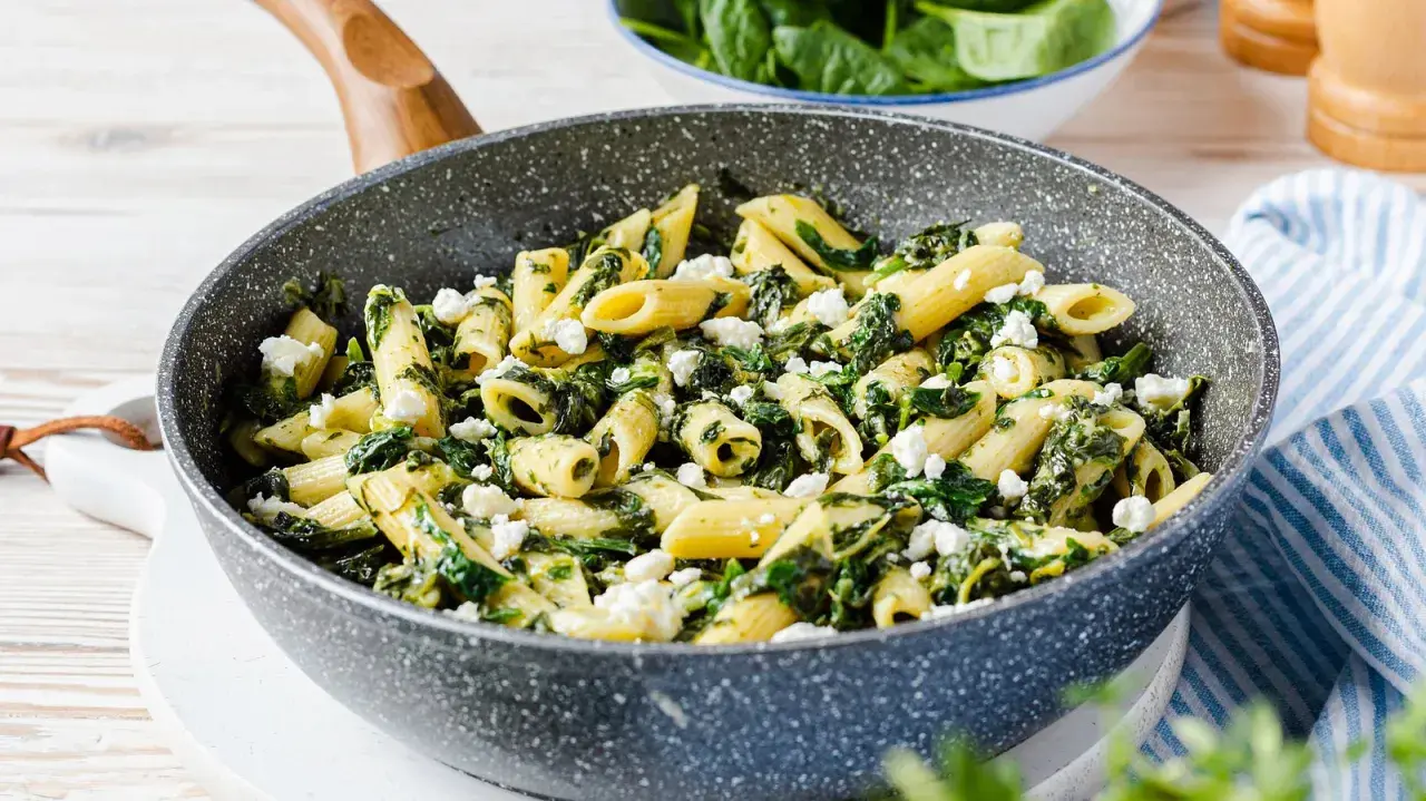Penne-Nudeln mit Spinat und zerbröseltem Feta in einer Pfanne.