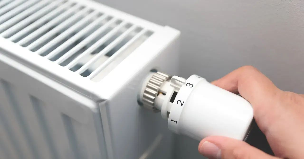 Dłoń kręci termostatem grzejnika, ustawiając temperaturę. Czas zacząć sezon grzewczy.