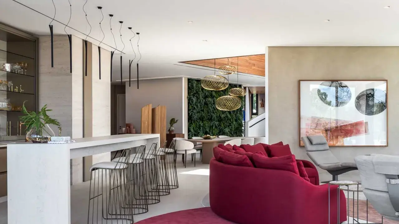 Elegante sala con barra y taburetes, una pared verde y una lámpara quinqué techo que ilumina el espacio.