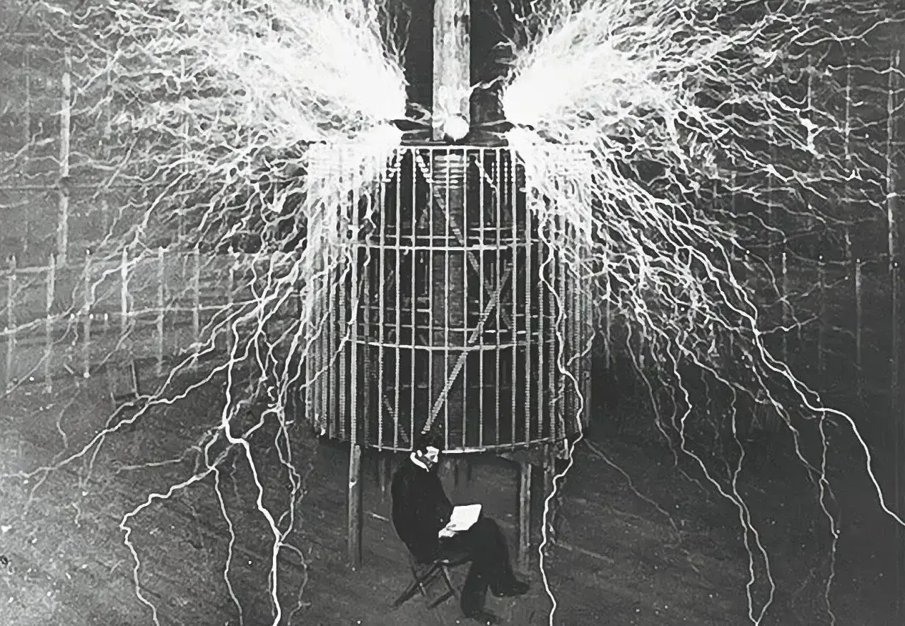 Nikola Tesla w klatce, otoczony wyładowaniami elektrycznymi, badał, kto wynalazł prąd.
