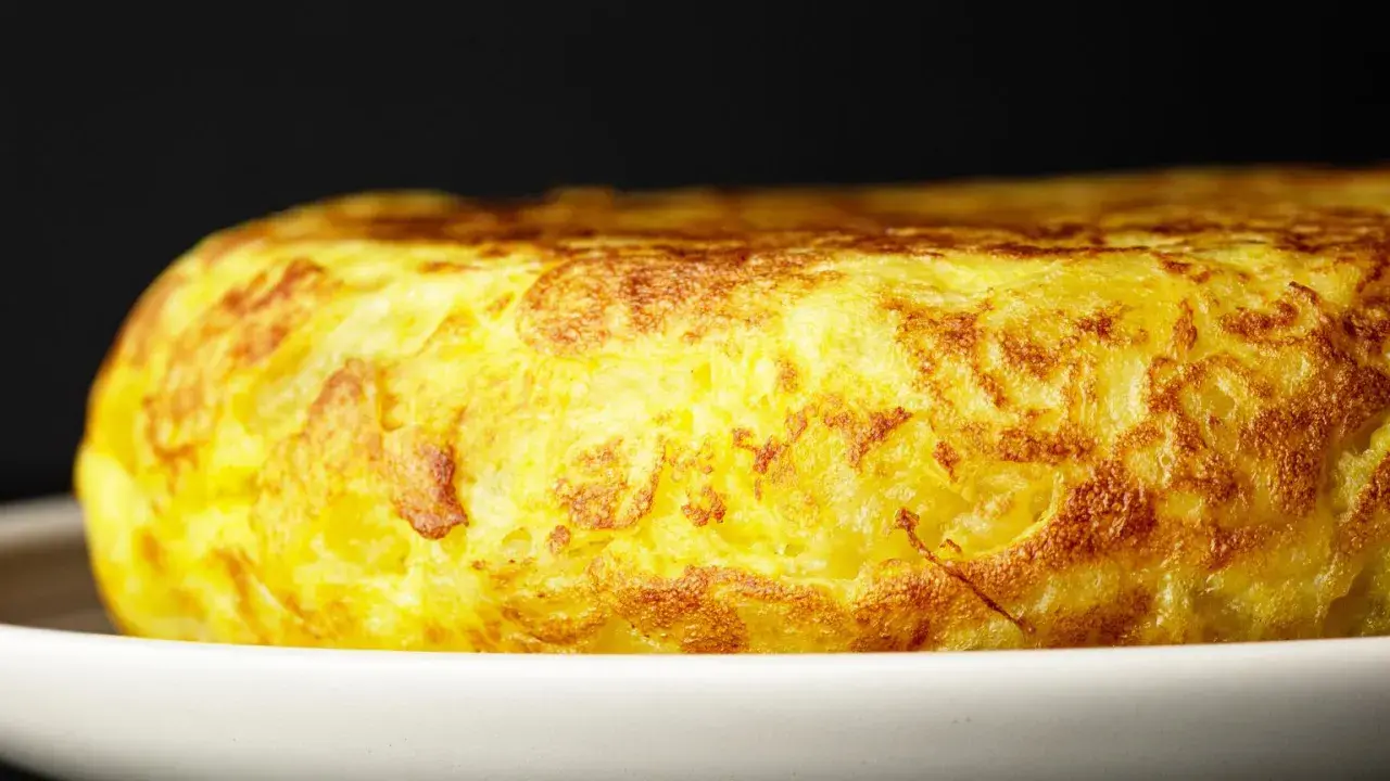 Złocista tortilla de patatas, pachnąca ziemniakami i jajkami, kusi apetycznym wyglądem na białym talerzu.