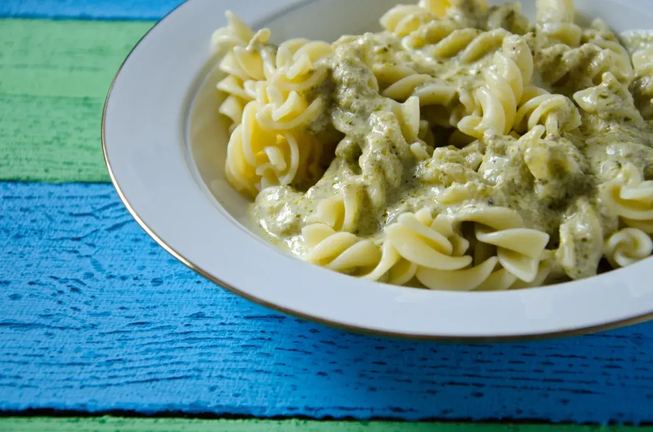 Fusilli-Nudeln in cremiger Pesto Sahne Sauce, serviert auf einem bunten Holztisch.