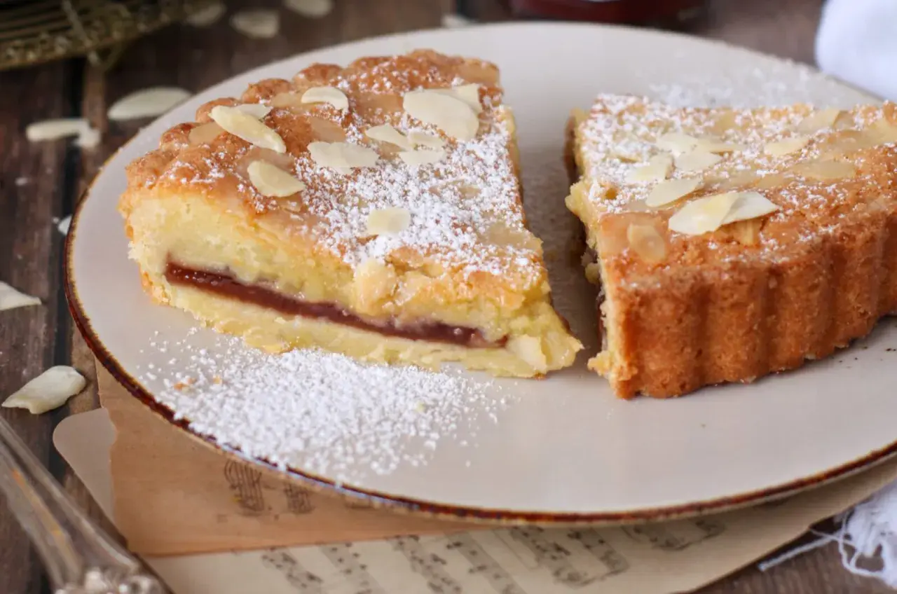 Fette di crostata frangipane con marmellata e mandorle, spolverate di zucchero a velo.