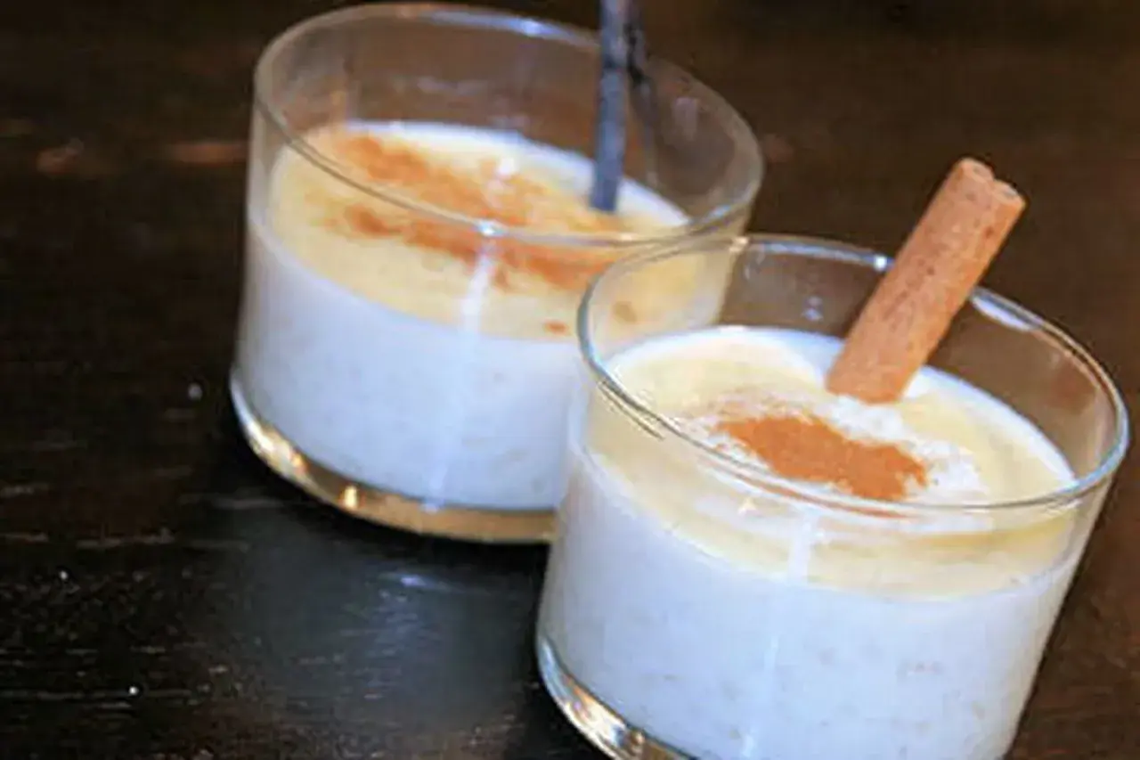 Deux verres de riz au lait crémeux, saupoudrés de cannelle. Un bâton de cannelle décore l'un des desserts, parfait pour une recette de riz au lait.