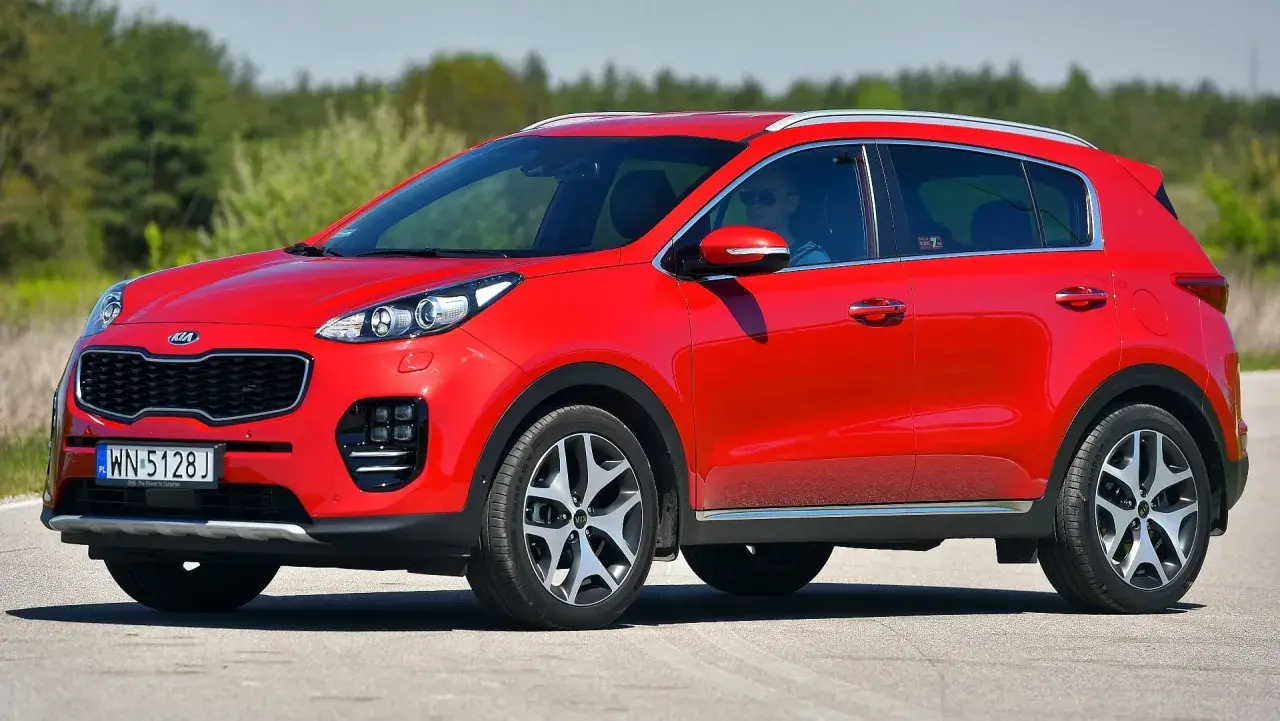 Czerwony Kia Sportage 1. generacji z kierowcą w okularach przeciwsłonecznych jedzie po drodze.