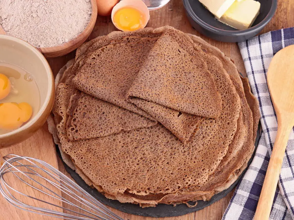 Pile de crêpes de sarrasin, avec des ingrédients pour la pâte à crêpe sarrasin : farine, œufs, beurre.