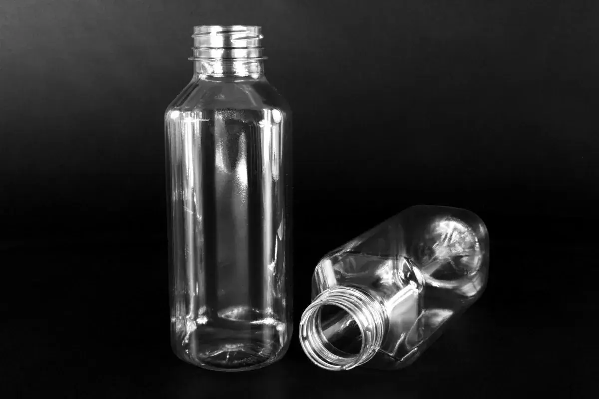Dwie puste, przezroczyste butelki PET o pojemności 300 ml na czarnym tle. Jedna stoi pionowo, druga leży.