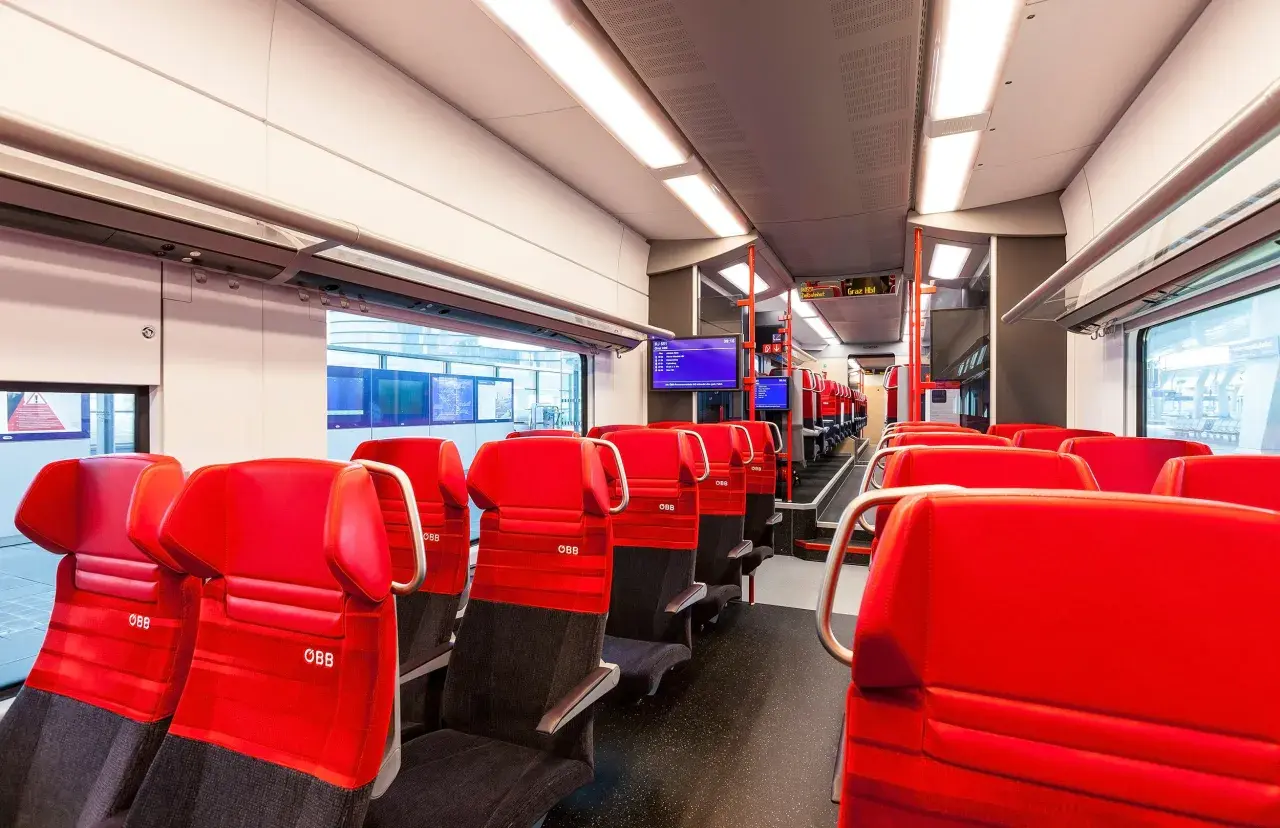 Rote Sitze im modernen Desiro ML Zug der ÖBB. Die Sitze sind mit dem ÖBB-Logo versehen und laden zu einer angenehmen Reise ein.