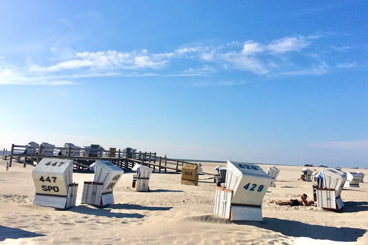 Strandkörbe am St. Peter-Ording Strand unter blauem Himmel. Eine Person entspannt sich im Sand.