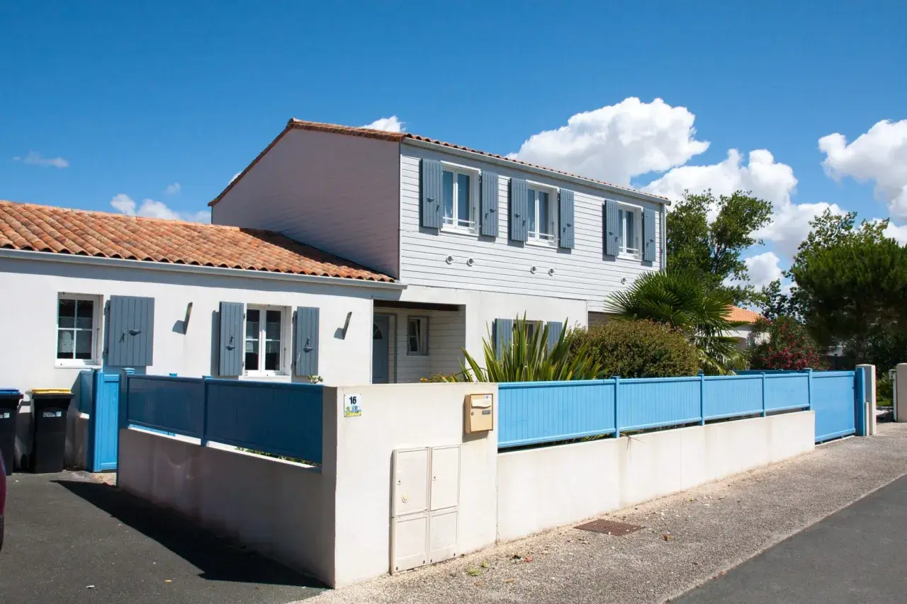 Maison année 70 rénovée, avec volets bleus et clôture assortie. Avant, elle était plus sombre.