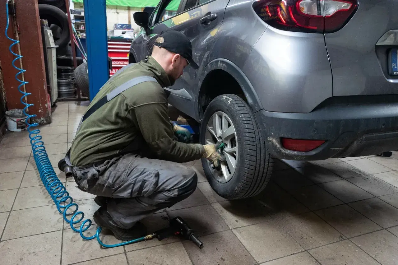 Mechanik wymienia koło w samochodzie. Czy w Polsce obowiązują opony zimowe? To pytanie zadaje sobie wielu kierowców przed sezonem.