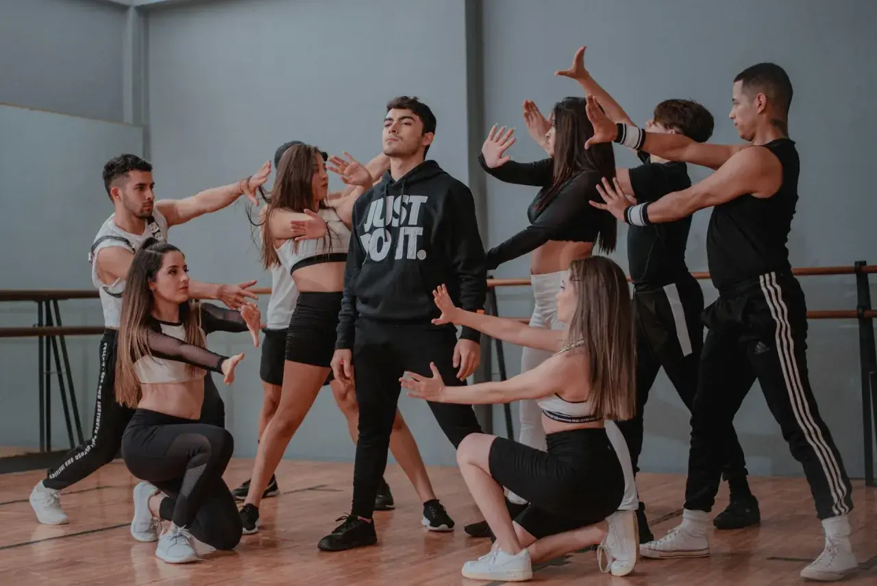 Un gruppo di giovani ballerini in abiti sportivi esegue una coreografia di danza pop in uno studio.