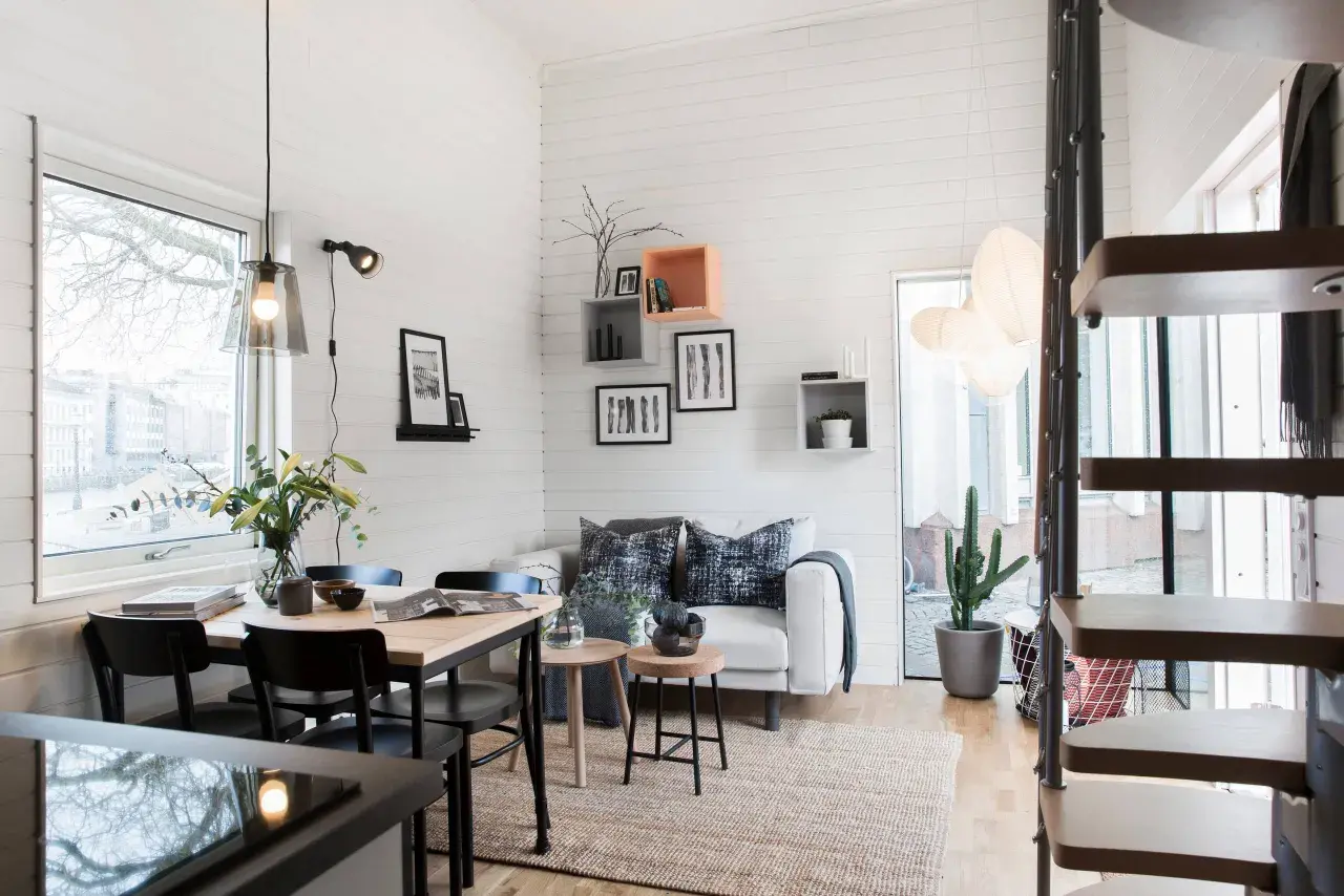 Mysig inredning i ett attefallshus med soffa, matbord och en spiraltrappa.