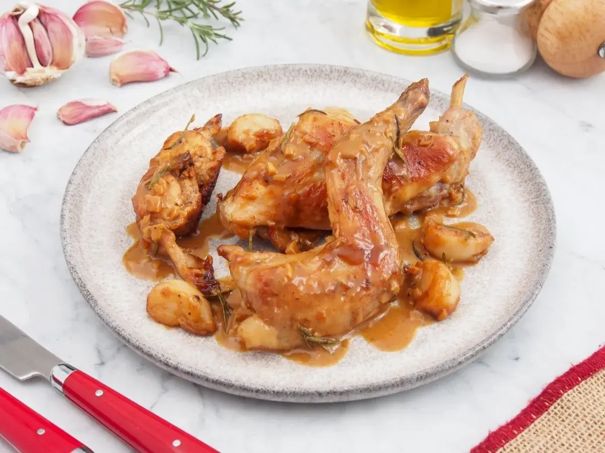 Delicioso conejo al ajillo servido en un plato, con ajos enteros y romero. Una receta tradicional lista para disfrutar.