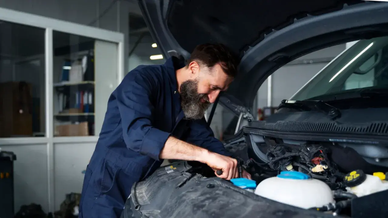Mechanik z brodą pracuje przy silniku. Zastanawiasz się, ile kosztuje wymiana chłodnicy w samochodzie?