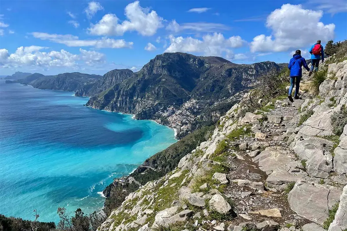 Hikers on the "walk of the gods" trail, with stunning turquoise waters and coastal villages below.