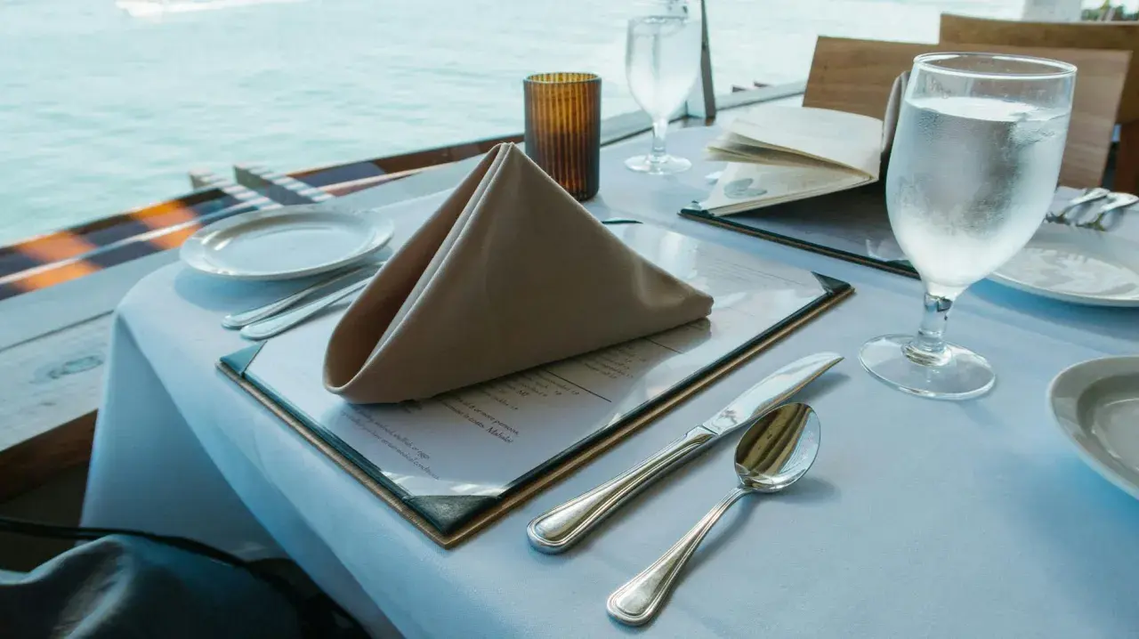 Stół w restauracji z widokiem na morze, nakryty do posiłku, z menu i kieliszkiem wody.