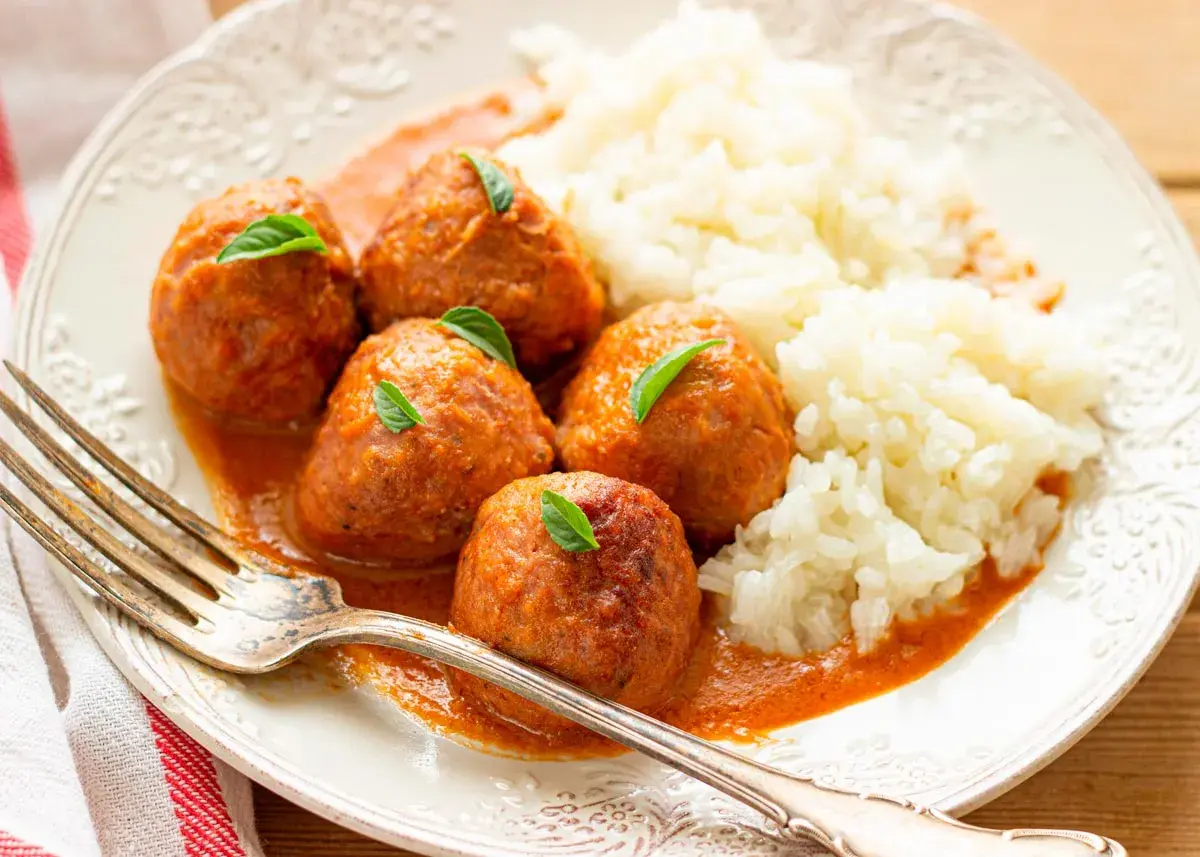 Albondigas a la jardinera con arroz blanco, decoradas con hojas verdes. Un plato casero y apetitoso.