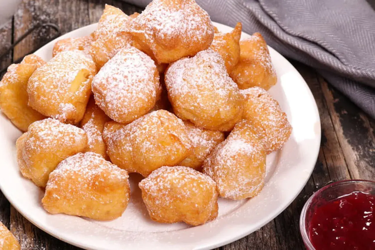 Une assiette de beignets banane saupoudrés de sucre glace, prêts à être dégustés avec une confiture de fruits rouges.