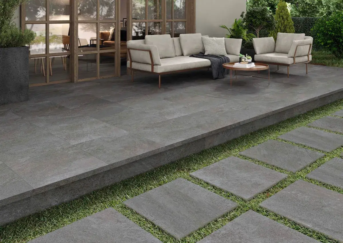 Terraza moderna con suelo de baldosas grises, ideal para pintar y renovar tu espacio exterior. Muebles de exterior y plantas verdes.