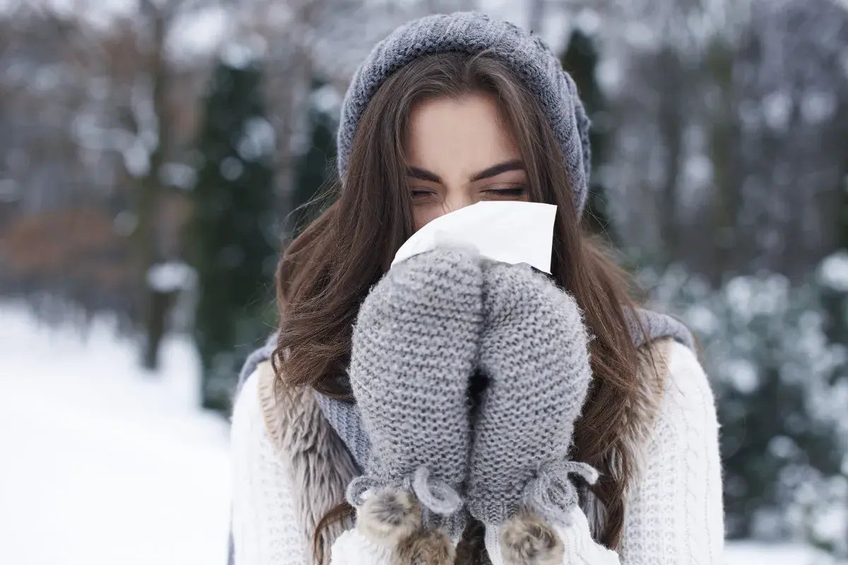 Femme en bonnet et moufles d'hiver se mouchant, un rappel pour prévenir le rhume.