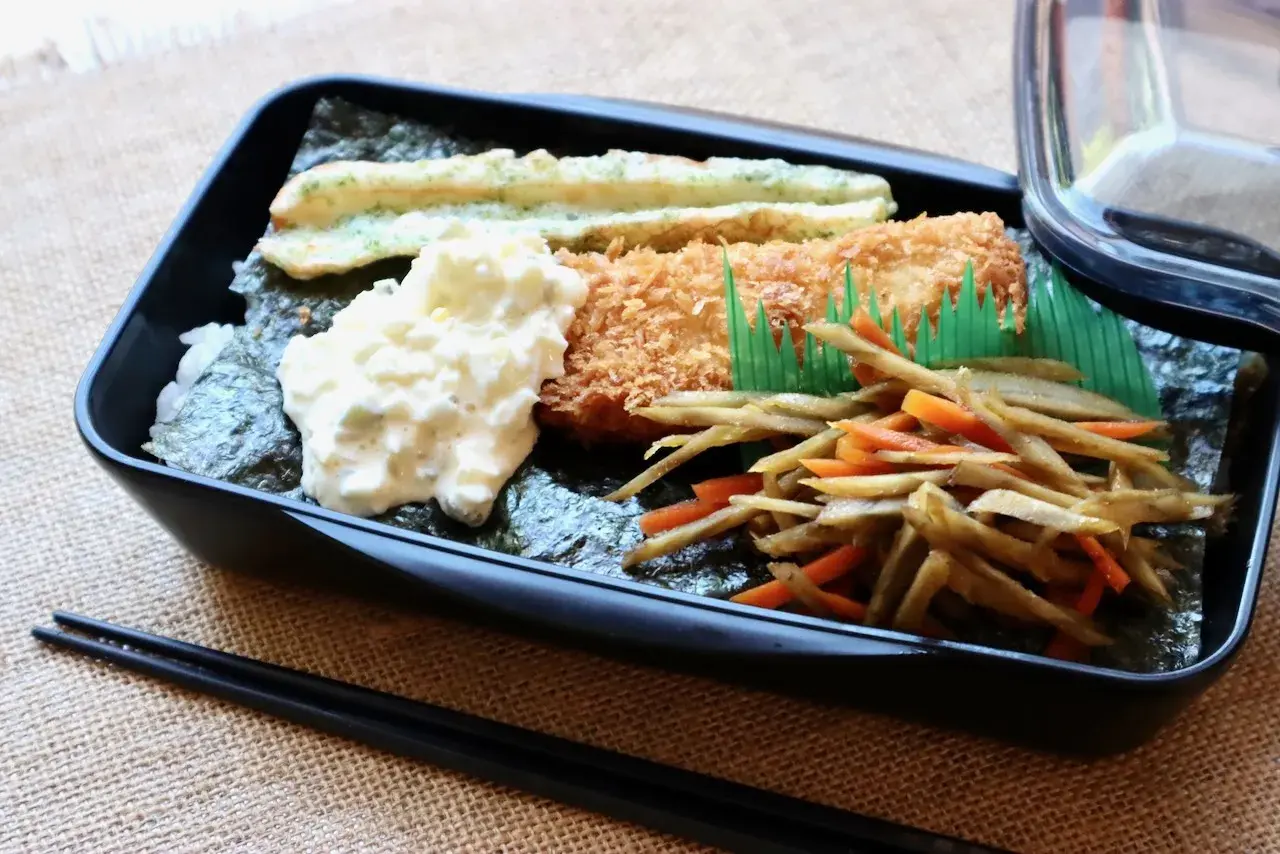 A delicious nori bento box with fried fish, creamy potato salad, and stir-fried vegetables.
