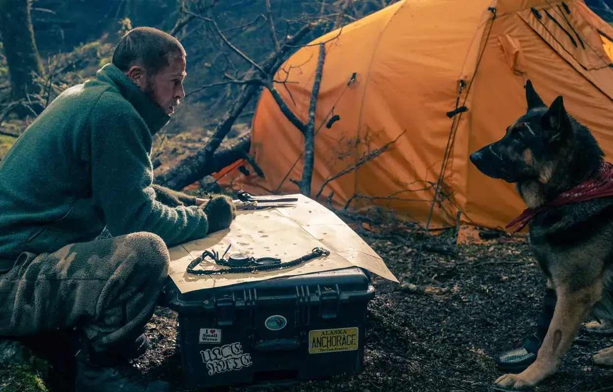 Man och hund vid orange tält, planerar en expedition. Kanske är det hjärtat av besten de söker.