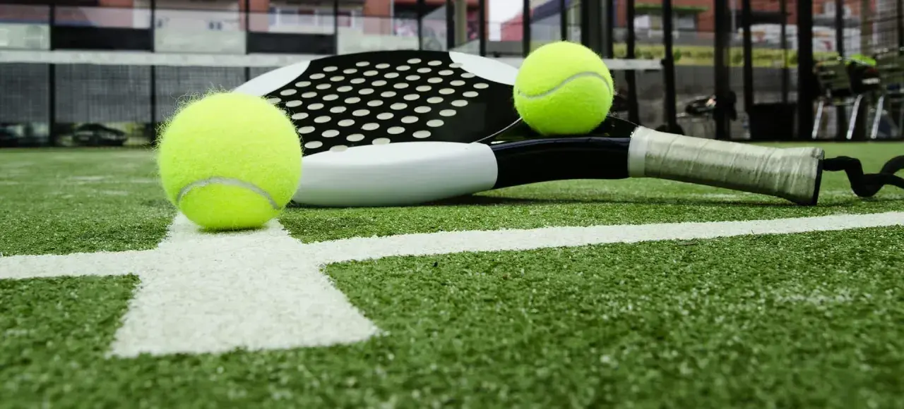 Raqueta de pádel y pelotas sobre césped artificial padel. La cancha está lista para el juego.