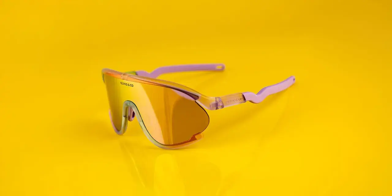 Oto odpowiedź na pytanie: jakie okulary na rower? Stylowe, pomarańczowe okulary sportowe z fioletowymi zausznikami, idealne na rowerową przejażdżkę.