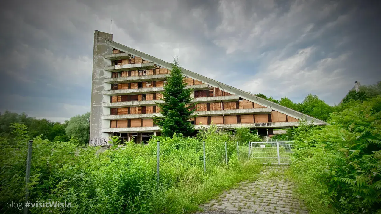 Opuszczony budynek o trójkątnym kształcie, z oknami zabitymi deskami, otoczony bujną zielenią. Idealne urbex miejsca dla poszukiwaczy przygód.