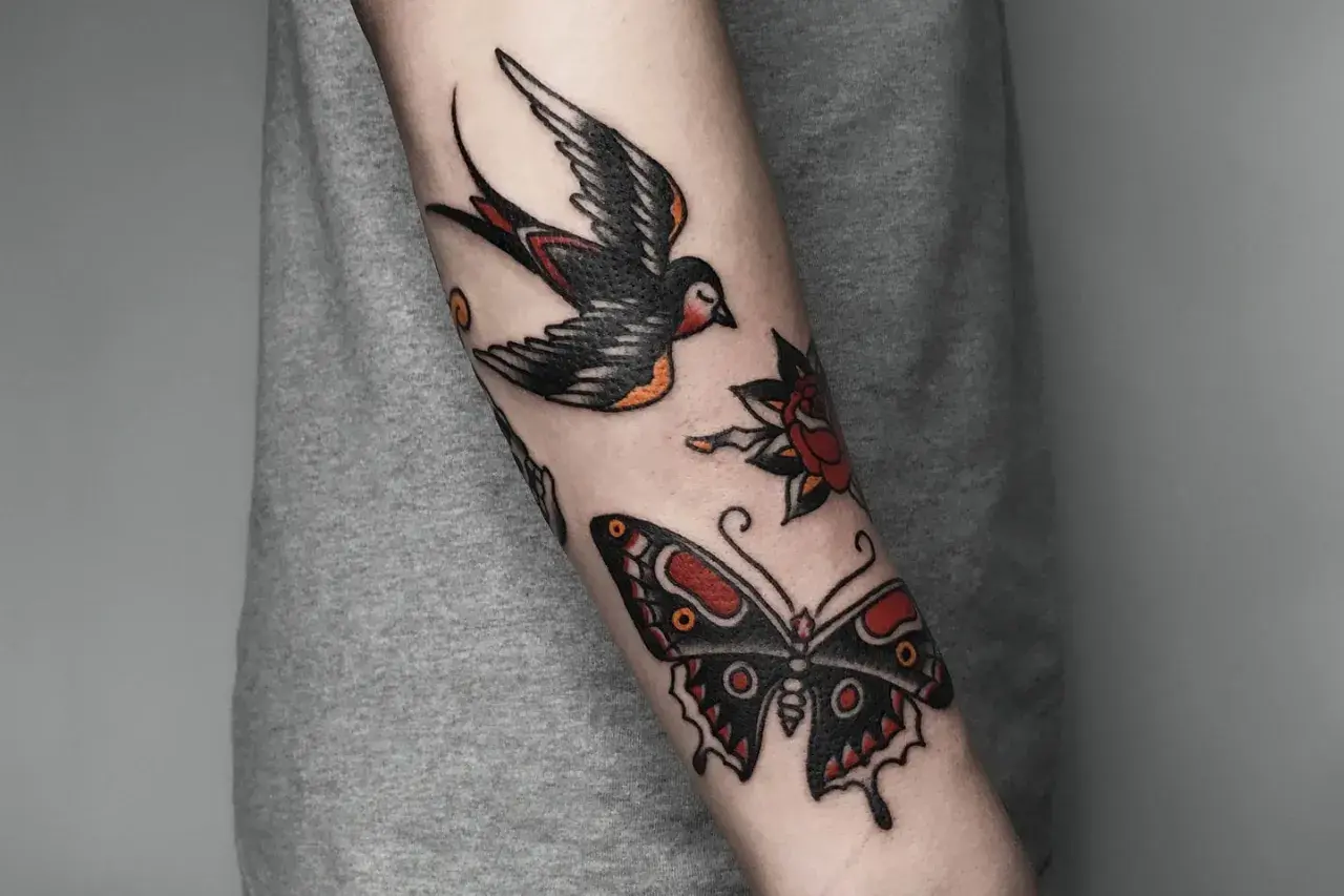 Tatuaż w stylu old school na przedramieniu: jaskółka, motyl i róża.