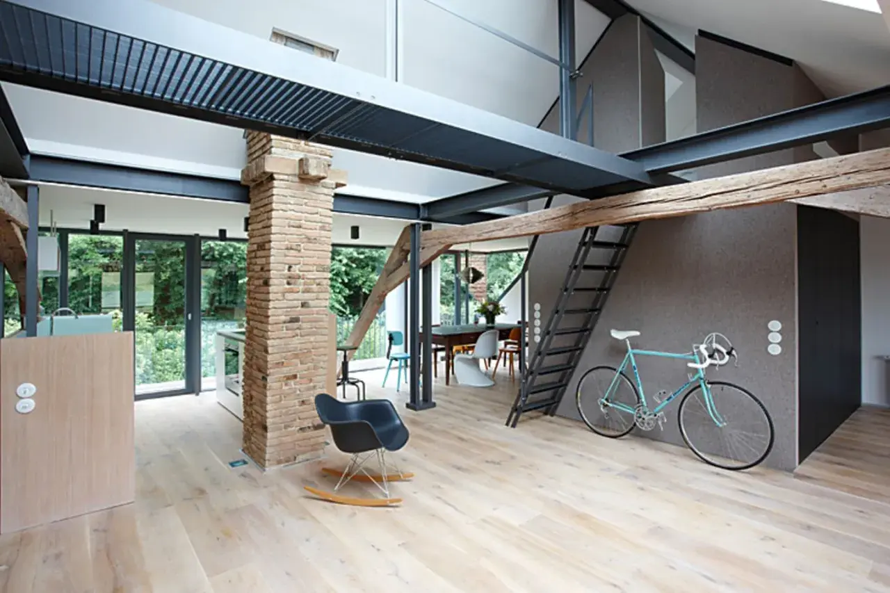 Moderner offener Dachstuhl mit sichtbaren Stahlträgern, Ziegelpfeiler, Holz und einer Leiter. Ein Fahrrad steht bereit.