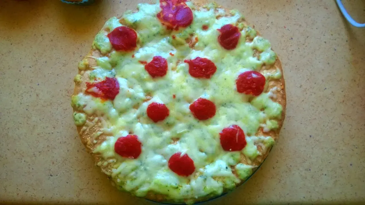 Domowa pizza z serem, zielonym sosem i czerwonymi kółkami pepperoni.