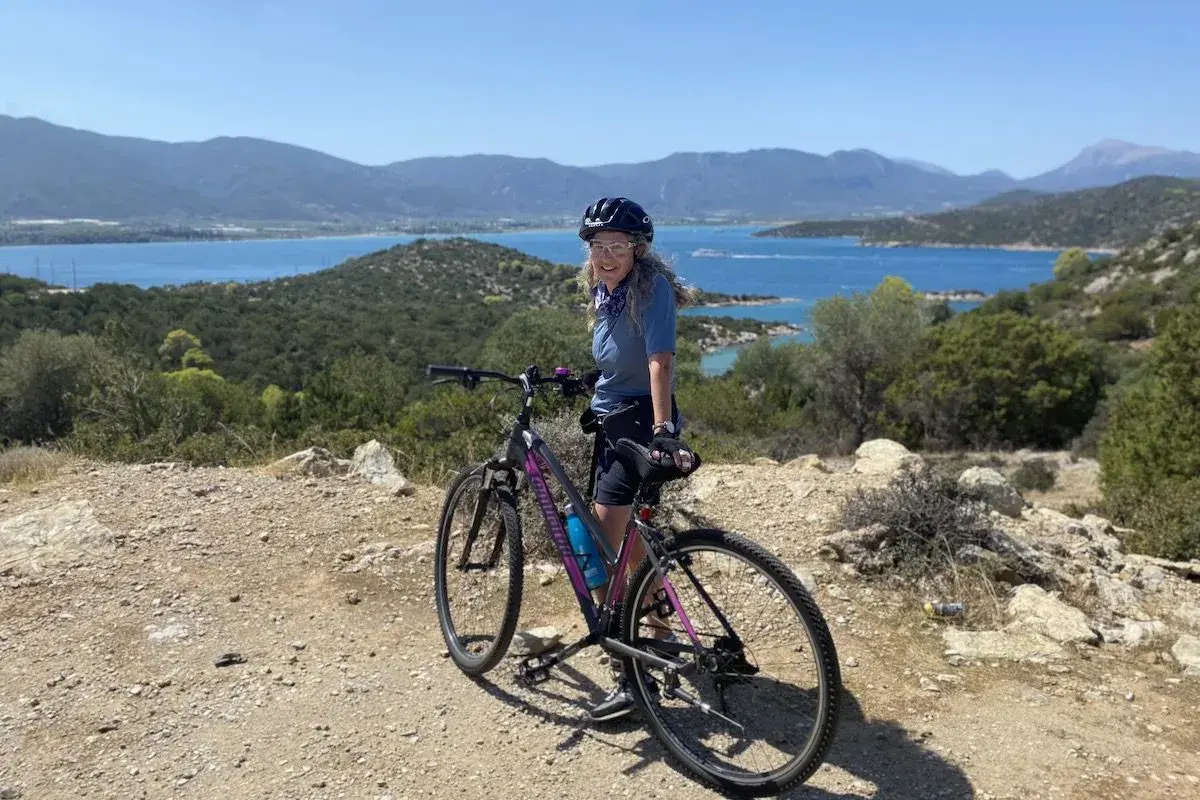 Woman on a bicycle enjoying scenic bicycle tours over 50, with a beautiful blue bay and mountains in the background.