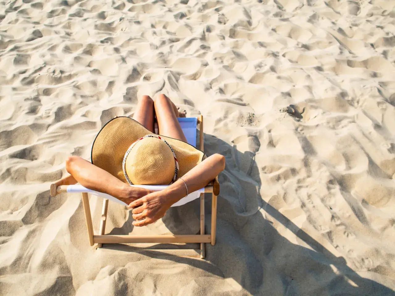 Relaks na plaży, idealne miejsce, gdzie na wakacje w lipcu. Kobieta w kapeluszu leży na leżaku wśród piaszczystych wydm.